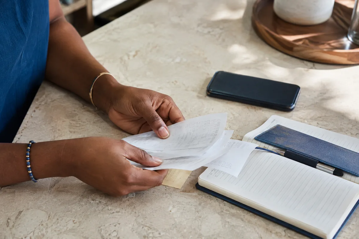 Hands reviewing payment receipts beside a phone and notebook on a business countertop.